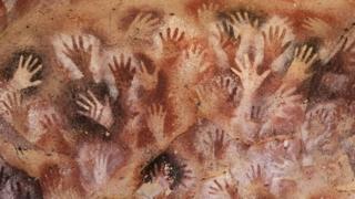 A series of handprints in red and white on a cave wall