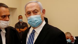 Israeli Prime Minister Benjamin Netanyahu, wearing a mask, stands inside the courtroom as his corruption trial opens on 24 May 2020