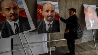 A man examines three color portraits of Vladimir Lenin