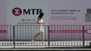 一位女土在港鐵紅磡站改建工程的圍板前走過(BBC News中文圖片9/8/2018)