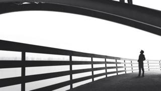 Una persona, a contraluz, caminando por un puente, y mirando a su alrededor, como perdida