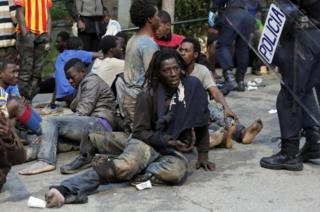 Мигранты сидят на земле рядом с испанскими полицейскими после штурма забора для входа в испанский анклав Сеута 17 февраля 2017 года