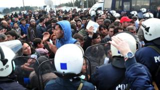 Police officers stand guard as migrants and refugees wait to cross the Greek-Macedonian border near the village of Idomeni, on March 2, 2016