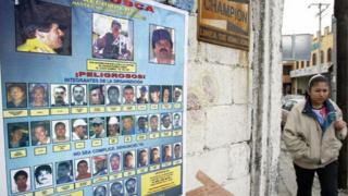 Mulher passa ao lado de cartaz de traficantes procurados