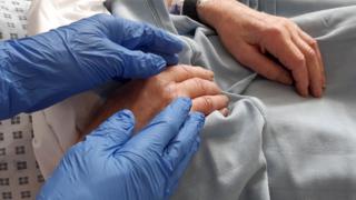 An NHS worker wearing gloves holds the hand of a Covid-19 patient