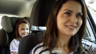Una mujer conduciendo un auto y una niña atrás