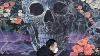 A man wears a protective face mask as he walks in front of a mural of skulls and flowers in New York