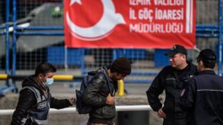 На этом файле, сделанном 8 апреля 2016 года, изображен сотрудник полиции, сопровождающий мигранта с турецкого парома, перевозящего вторую группу мигрантов, депортированных из Европы в Турцию, когда они прибывают в порт района Дикили в Измире. Турция 15 марта 2017 года