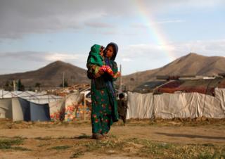 A displaced Afghan girl carries a child near their shelter at a refugee camp