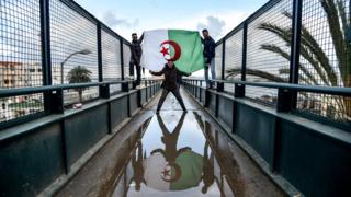 Алжирцы в драпированном государственном флаге принимают участие в демонстрации против больного президента Абдельазиза Бутефлики в столице Алжира 22 марта 2019 года.