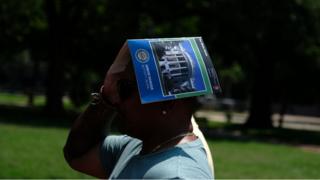 A tourist uses a guide book to cover their head
