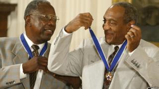 Actor Comedian Bill Cosby (right) jokes with baseball great Hank Aaron after they both received the Presidential Medal of Freedom Award from U.S. President George W. Bush during a ceremony 9 July 2002