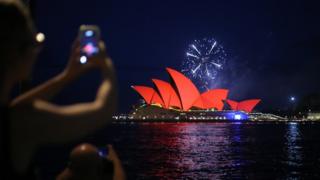 Spectators take pictures of fireworks as they explode behind the Sydney Opera House while they glow red as part of the Chinese Lunar New Year celebrations of the pig, to Sydney