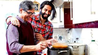 Mid adult man is looking over his father's shoulder as he prepares a curry at home