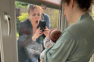 Frau sieht überglücklich aus, als sie ein Baby durch ein Fenster fotografiert