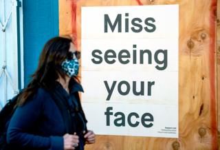 A woman in a face mask walks past a sign