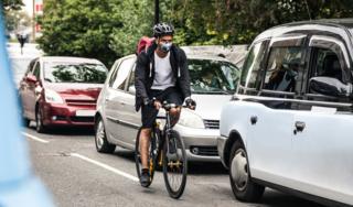 A stock image of a cyclist riding past cars