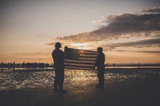 People dressed as US soldiers hold the US flag on Omaha beach
