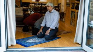 Misba Ahmed, a member of the Wapping Mosque, prays on prayer mats at home with his two sons, Mansur, 19, and Mushir, 17, during the coronavirus lockdown in Wapping, east London