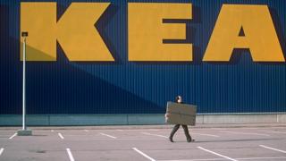 Man walking with a box in front of ikea sign