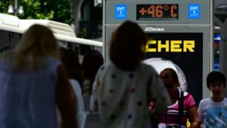People walk past a city digital board indicating 46 degrees Celsius at a bus stop in Madrid