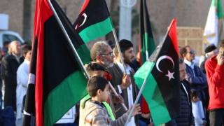 أشخاص من فئات عمرية مختلفة يحملون العلم الليبي