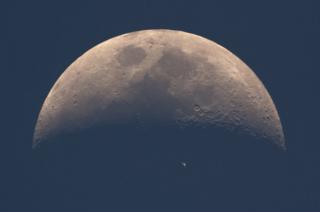 The International Space Station (ISS) whizzes across the dusky face of the moon