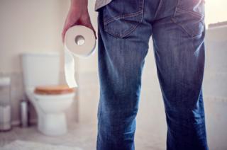 Hombre en un baño con rollo de papel en la mano