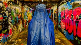 Muir's subject stands in a concrete basement covered in graffiti.