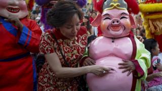 A woman puts money in the belly of an interpreter in pig costume during a lunar new year, or spring festival, in Chinatown