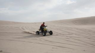 A man drives through the dunes on a quad bike