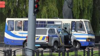 Ukrainian law enforcement officers lie on the ground behind a car near a passenger bus, which was seized by an unidentified person in the city of Lutsk, Ukraine July 21, 2020