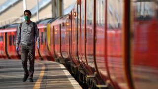 A passenger wearing a mask and gloves walks on the platform of the train