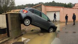 Residents stand next to a car washed away by the floods of October 15, 2018 in Villegailhenc, near Carcassone, in the south of France. - Six people died after a storm and sudden floods in the night of October 15 in the department of Aude, in southern France, authorities said.