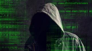 Una persona con una capucha, contra un fondo de códigos de computación.