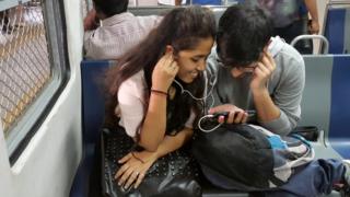 На этом снимке, сделанном 7 марта 2017 года, показаны индийские студенты, которые смотрят фильм на своем смартфоне во время поездки на пригородном поезде в Мумбаи. Выкупы, слияния и быстрые выходы - поскольку самый богатый человек Индии встряхивает ультраконкурентный рынок мобильной связи в стране, телекоммуникационные компании пытаются либо консолидировать, либо сократить свои потери и бежать.