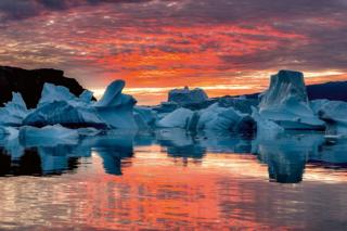 A sunrise over a number of icebergs
