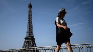A woman walks on a bridge over the Seine river in front of the Eiffel tower in Paris on July 24, 2019