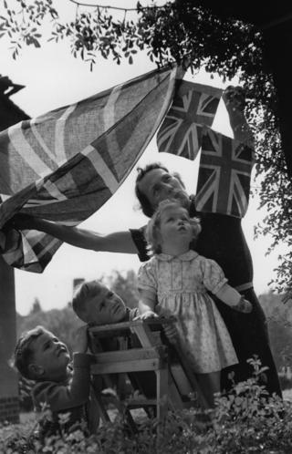 Children help put up bunting and flags on VE Day in London