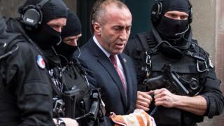 Бывший премьер-министр Косово Рамуш Харадинай (в центре) покидает суд в сопровождении полицейских в капюшонах в Кольмаре, восточная Франция
