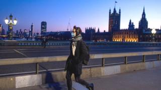 A man wearing a mask crosses Westminster Bridge past the Houses of Parliament
