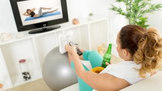 Una mujer viendo un programa deportivo con una bebida en la mano