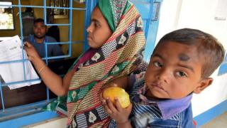 শিশু কোলে নিয়ে এক নারী তালিকায় তার নাম খুঁজছেন।