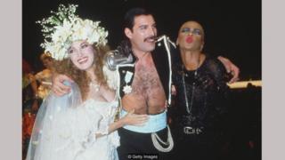 Jane Seymour dalam gaun Emanuel, bersama Freddie Mercury dan seorang teman di acara amal Fashion Aid pada 1985.