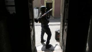 a man in combat gear standing in a doorway holding a weapon