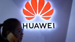 Pessoa fala ao telefone em frente a logo da Huawei
