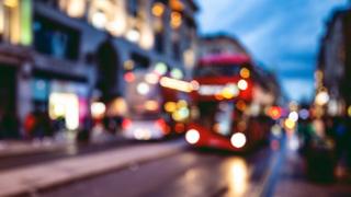 A bus approaches a stop on a London street at night