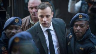 Oscar Pistorius arrives at court wearing a suit, flanked by two guards