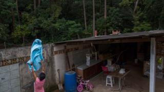 Mulher coloca roupa no varal em casa perto de mata