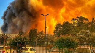 A massive blaze is seen over residential houses and parked cars in Forster on 7 November 2019